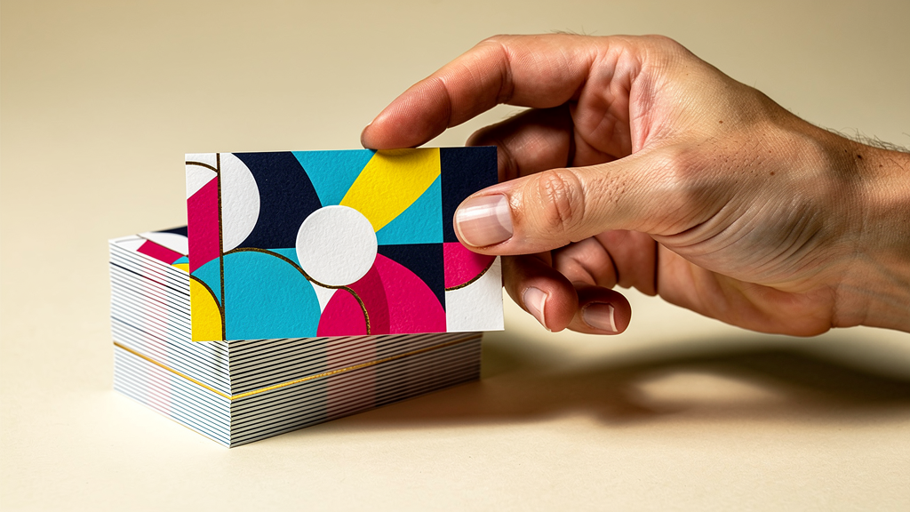 A hand holding a premium business card above a precisely cut stack